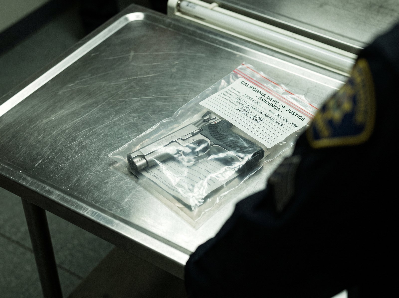 Close-up of a handgun in an evidence bag on a metal table, California law enforcement, late 1990s, archival editorial style, the working tool of the California Unsafe Handgun Act.