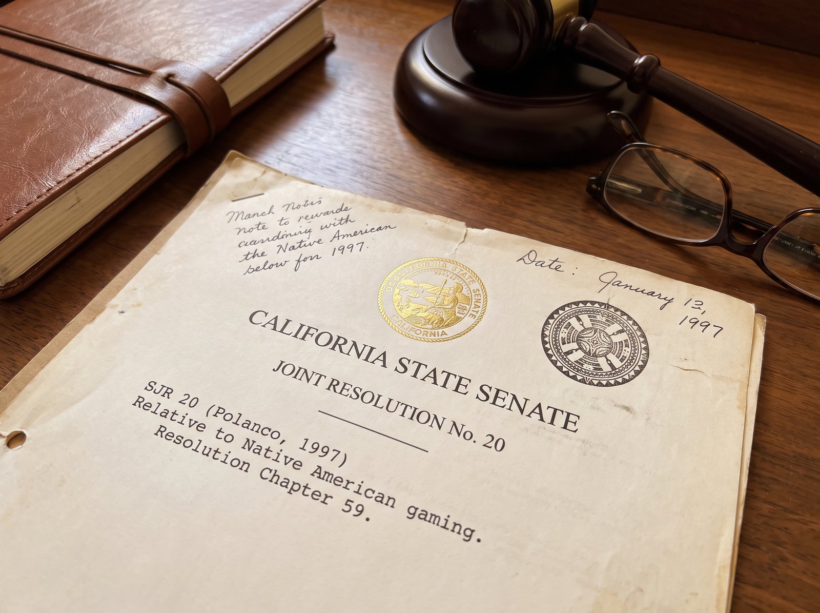 Close-up of a California State Senate joint resolution document on a legislative desk, with the California state seal and a Native American tribal seal, late afternoon light, archival editorial style, the working instrument of the California State Senate joint resolution.