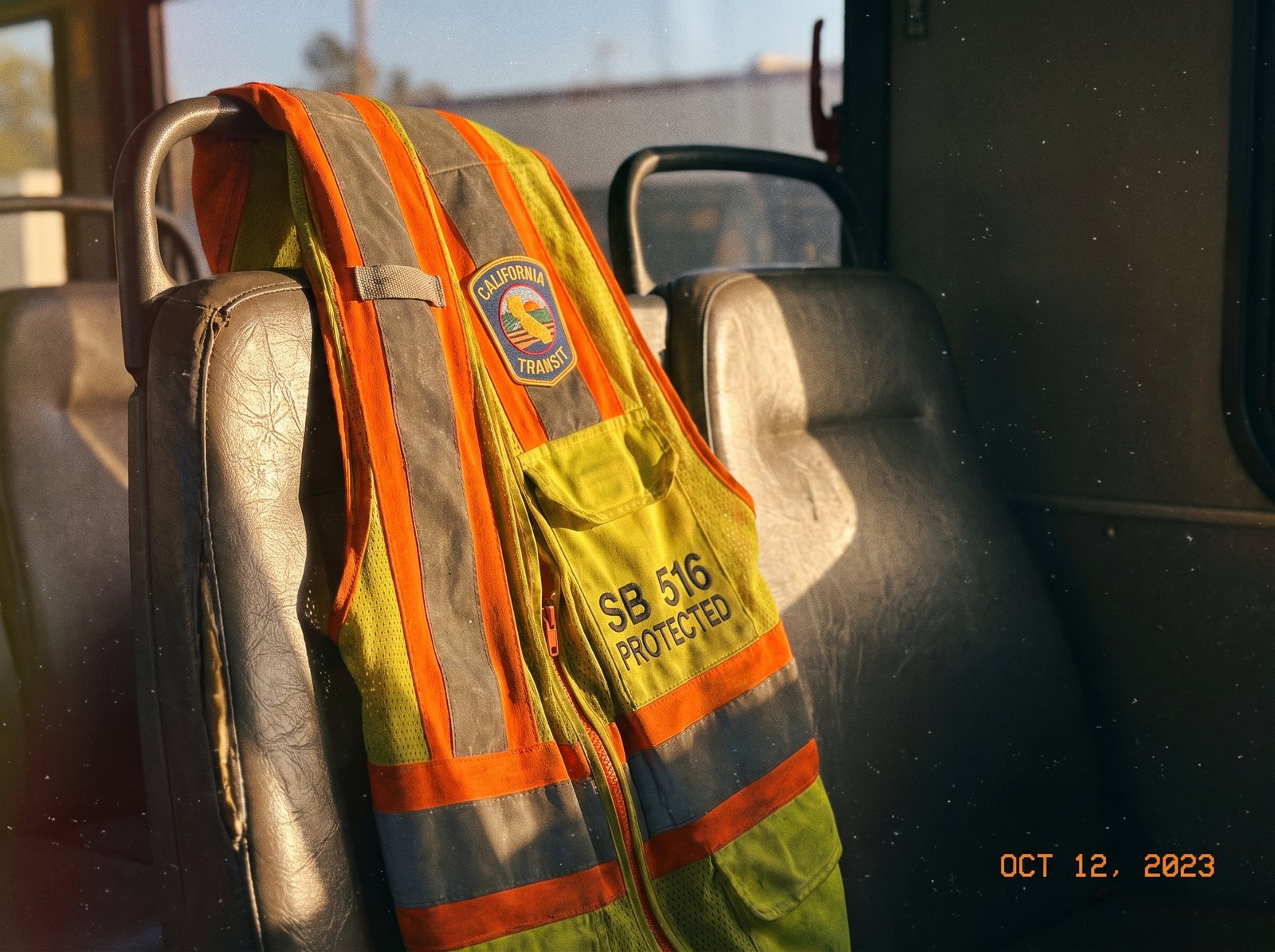 Close-up of a transit operator safety vest hanging on the back of a bus seat, late afternoon light, archival editorial style, the working garment of the California transit bus operator protected by SB 516.